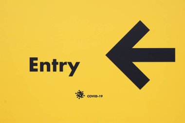 Coronavirus uyarı işareti. Üzerinde COVID-19 karantina ve virüs sembolü yazılı plaka, sarı arka planda siyah. ok işareti ve koronavirüs işareti