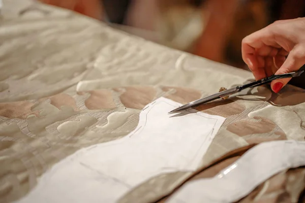 Makasla el, açık bej kumaşla kağıt kesimi. Kesme işleminin yakın plan resmi. Dikiş dersi. Moda tasarımcısından model oluşturma atölyesi.