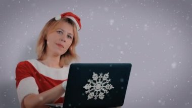 Noel Baba gibi giyinmiş bir kız dizüstü bilgisayarda yeni yılını kutluyor. Beyaz arkaplan, düşen kar.