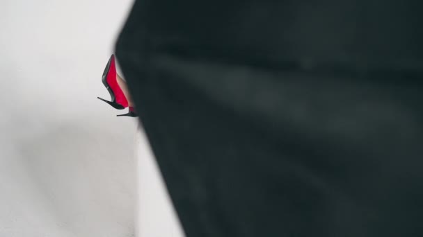 一个白人女人穿着漂亮的红鞋子 躺在白色的沙发上靠着一面白墙 骑着滑翔机 把滑翔机从烟道后面拿出来 — 图库视频影像