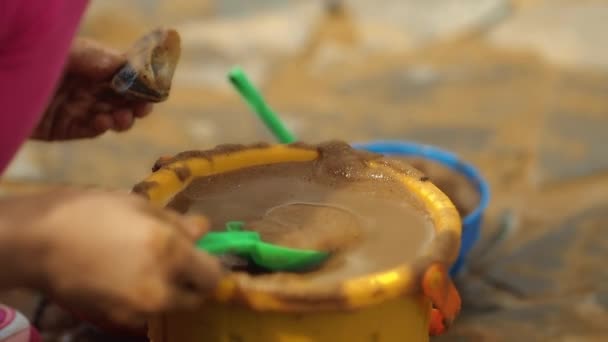 Dos niñas juegan con arena y agua. Tienen un cubo amarillo y una cucharada. Día soleado . — Vídeos de Stock