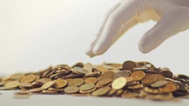 Beyaz eldivenli eller bir yığın altın madeni parayı topluyor. Para dağıtırlar. Beyaz arka planda..