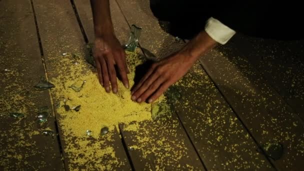 Les mains d'un homme caucasien prennent un gros plan de millet jaune du sol. À côté du verre cassé . — Video