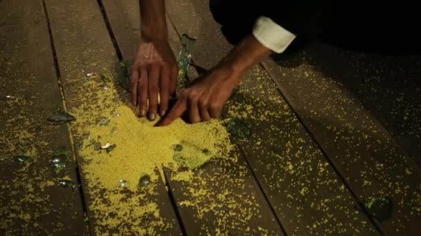 白人男性の手は床から黄色のキビのクローズアップを取ります。壊れたガラスの隣に. — ストック動画
