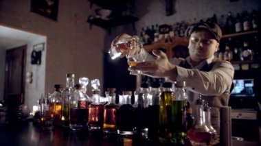 The bartender pours whiskey into a tasting glass (glencairn).  A bar counter in the speakeasy style. Dark scene, slow motion, camera movement.