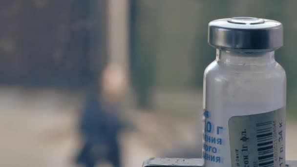 A medicine bottle in the foreground. People are walking down the street in full focus. Quarantine. — Stock Video