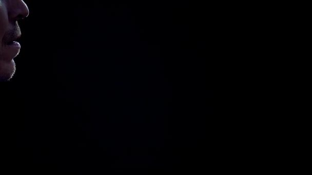Un homme caucasien en t-shirt blanc éternue sur un fond noir. Des gouttes de pulvérisation sont visibles dans la lumière de fond . — Video