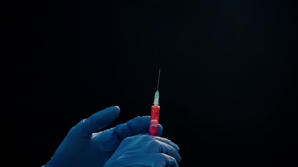 Een hand in een blauwe medische handschoen houdt een spuit voor injectie vast. Schud luchtbellen af. Controleren van de spuit, de drug jet. — Stockvideo