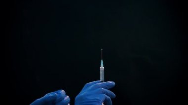 Mavi tıbbi eldivenli bir el enjeksiyon için bir şırınga tutar. Hava kabarcıklarından kurtulur. Şırıngayı ve uyuşturucu jetini kontrol ediyorum..