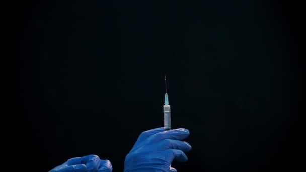 Een hand in een blauwe medische handschoen houdt een spuit voor injectie vast. Schud luchtbellen af. Controleren van de spuit, de drug jet. — Stockvideo