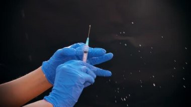 Mavi tıbbi eldivenli bir el enjeksiyon için bir şırınga tutar. Hava kabarcıklarından kurtulur. Şırıngayı ve uyuşturucu jetini kontrol ediyorum..