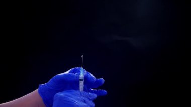 Mavi tıbbi eldivenli bir el enjeksiyon için bir şırınga tutar. Hava kabarcıklarından kurtulur. Şırıngayı ve uyuşturucu jetini kontrol ediyorum..