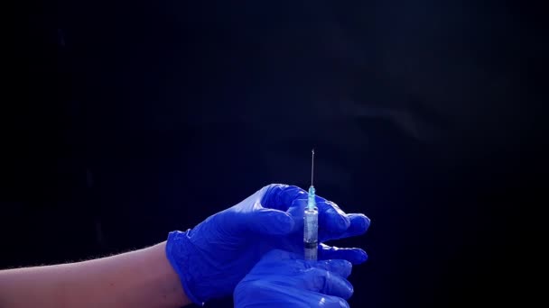 Een hand in een blauwe medische handschoen houdt een spuit voor injectie vast. Schud luchtbellen af. Controleren van de spuit, de drug jet. — Stockvideo