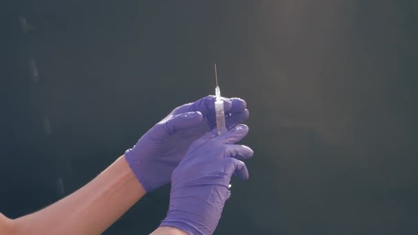 Een hand in een blauwe medische handschoen houdt een spuit voor injectie vast. Schud luchtbellen af. Controleren van de spuit, de drug jet. — Stockvideo