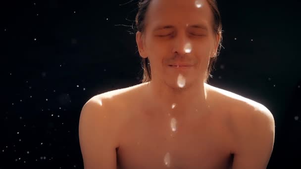 Un hombre caucásico, desnudo hasta la cintura, se lava la cara con un chorro de agua. Fondo negro, cámara lenta . — Vídeo de stock