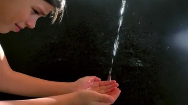 Kafkasyalı bir çocuk bir su akıntısı ile yüzünü yıkar. Siyah arka plan. Güneşler parlıyor.