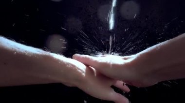 Beyaz bir adam ellerini bir su deresinin altında yıkıyor. Yavaş çekim su damlası püskürtüyor.