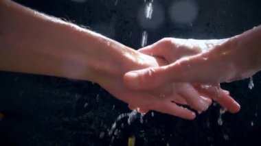 Beyaz bir adam ellerini bir su deresinin altında yıkıyor. Yavaş çekim su damlası püskürtüyor.