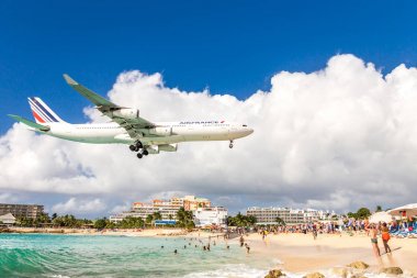 PHILIPSBURG, SINT MAARTEN - DECEMBER 13, 2016: A commercial airplane approaches Princess Juliana airport above onlooking spectators on Maho beach. clipart