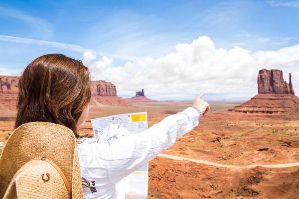 Back side of girl wearing straw hat searching right direction on map in Monument Valley, Utah, USA
