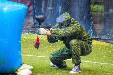 Koruyucu üniformalı ve maskeli bir paintball oyuncusu dışarıda silahla oynuyor.