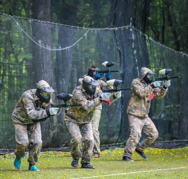 Koruyucu üniformalı ve maskeli bir paintball oyuncusu dışarıda silahla oynuyor.