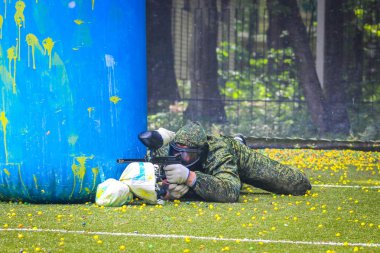 Koruyucu üniformalı ve maskeli bir paintball oyuncusu dışarıda silahla oynuyor.