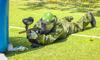 Koruyucu üniformalı ve maskeli bir paintball oyuncusu dışarıda silahla oynuyor.