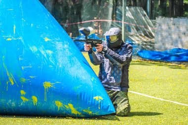 Koruyucu üniformalı ve maskeli bir paintball oyuncusu dışarıda silahla oynuyor.