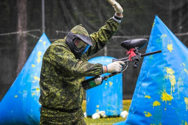 Koruyucu üniformalı ve maskeli bir paintball oyuncusu dışarıda silahla oynuyor.