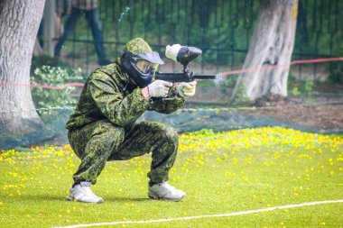 Koruyucu üniformalı ve maskeli bir paintball oyuncusu dışarıda silahla oynuyor.