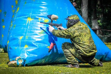 Koruyucu üniformalı ve maskeli bir paintball oyuncusu dışarıda silahla oynuyor.