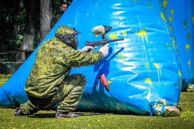 Koruyucu üniformalı ve maskeli bir paintball oyuncusu dışarıda silahla oynuyor.
