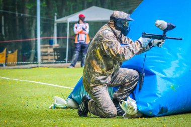 Koruyucu üniformalı ve maskeli bir paintball oyuncusu dışarıda silahla oynuyor.