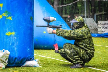 Koruyucu üniformalı ve maskeli bir paintball oyuncusu dışarıda silahla oynuyor.