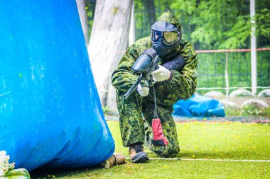 Koruyucu üniformalı ve maskeli bir paintball oyuncusu dışarıda silahla oynuyor.
