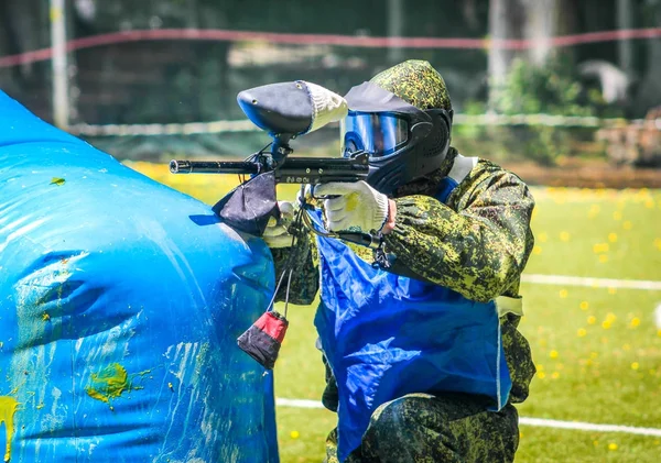 Koruyucu üniformalı ve maskeli bir paintball oyuncusu dışarıda silahla oynuyor.