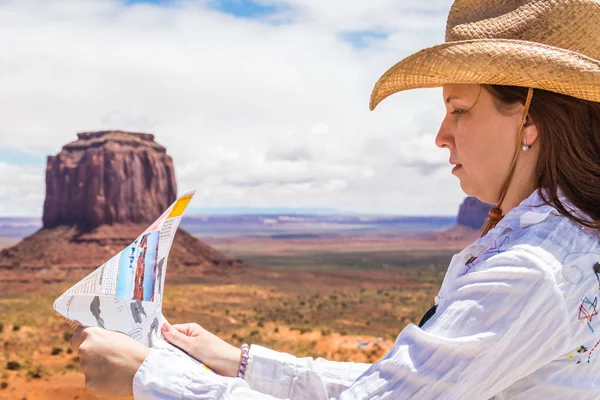 Back side of girl wearing straw hat searching right direction on map in Monument Valley, Utah, USA