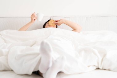 Yatakta battaniyenin altından bir fincan kahve tutan kadın. Sabah uyanan kadın