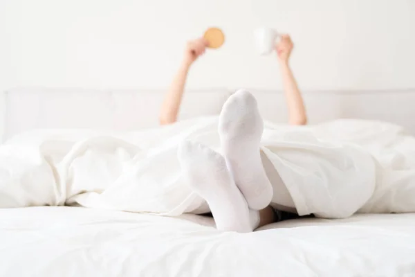 Женские ноги в белых носках под одеялом в постели. Женщина просыпается утром. — стоковое фото