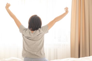 Genç bir kadın uyandıktan sonra yatakta geriniyor.