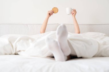 Yatakta battaniyenin altından bir fincan kahve tutan kadın. Sabah uyanan kadın