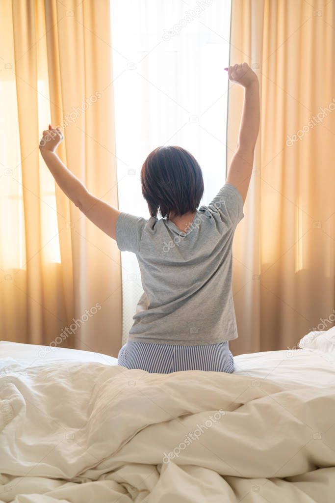 Woman stretching in bed after wake up, back view