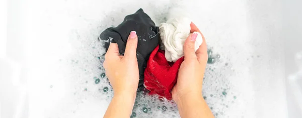 Panorama de manos femeninas lavándose la ropa negra, roja y blanca en espuma blanca —  Fotos de Stock