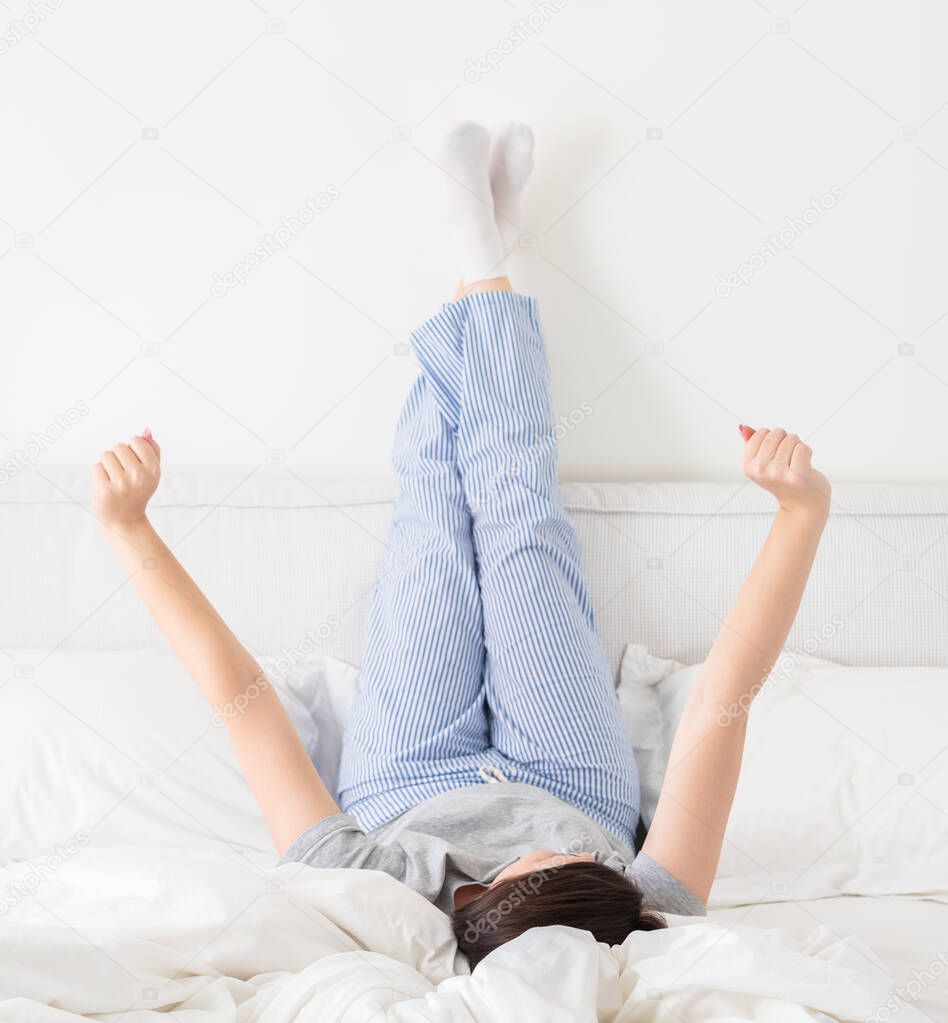 Yong woman in bed with legs up high against wall