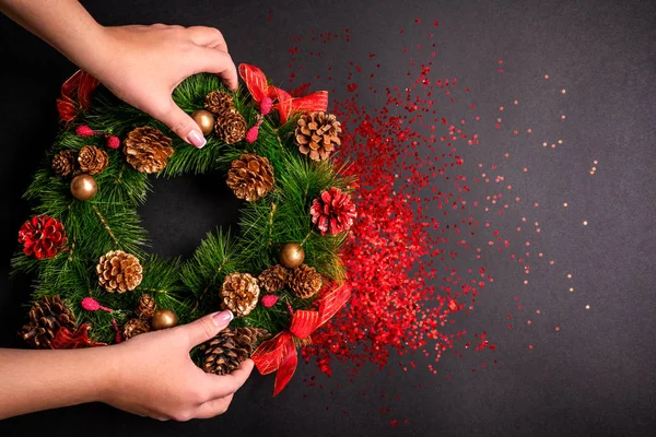 Female hands holding christmas wreath over black background with glitter and copy space — Stock Photo, Image