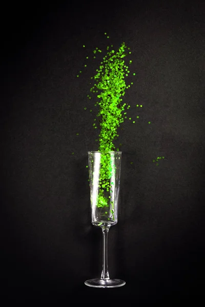 Glas met groene glitter op zwarte achtergrond, vlak bovenaanzicht — Stockfoto