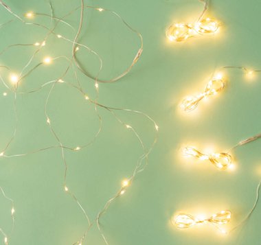 Açık yeşil arka planda Noel ışıkları, tatil çelengi ile yatıyordu