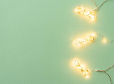 Açık yeşil arka planda Noel ışıkları, tatil çelengi ile yatıyordu