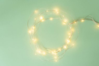 Açık yeşil arka planda Noel ışıkları, tatil çelengi ile yatıyordu